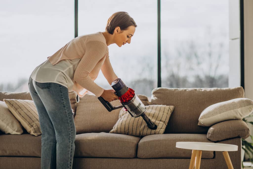 Young woman with rechargeable vacuum cleaner cleaning at home Person reinigt Stoffsofa mit Mikrofasertuch – effektive Tipps zur Polstermöbelpflege ohne Chemie