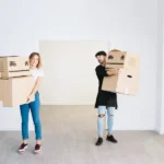 Ein Mann und eine Frau bringen nach dem Transport verpackte Möbel in die neue Wohnung.