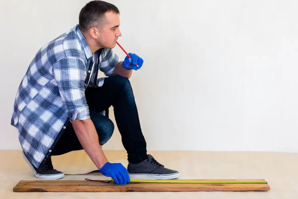 Im Vordergrund misst ein Mann beim Aufbau von Möbeln ein Teil.