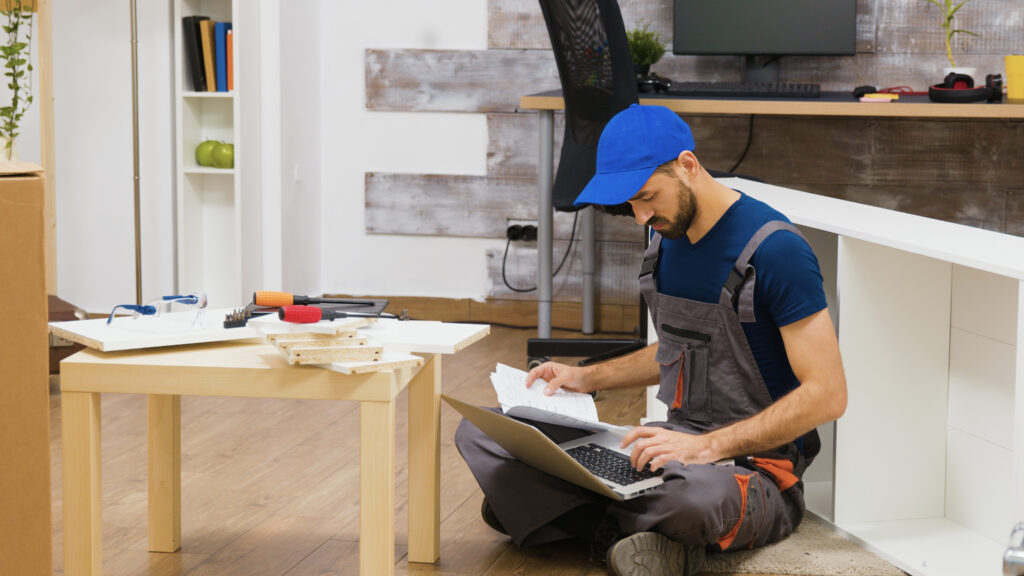 Furniture assembly worker uses laptop to consult instructions
