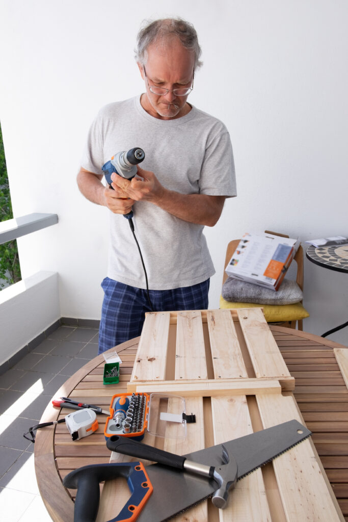 Grey-haired man in glasses holding electric screwdriver