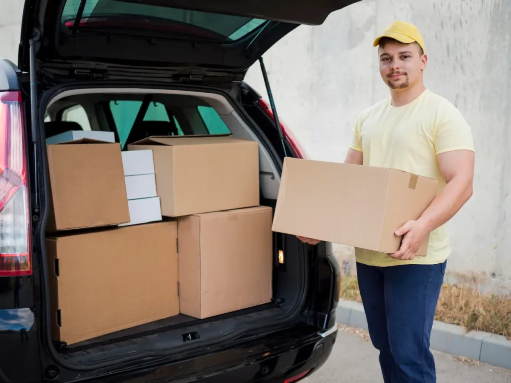 srednii-vystrel-paren-derzit-korobku Ein Mann lädt gepackte Sachen und Möbel für den Umzug in ein Auto.